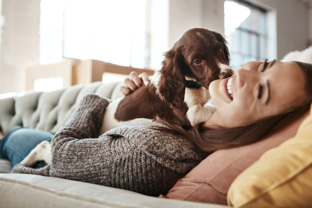 Une femme souriante et un chien sont allongés sur un canapé gris